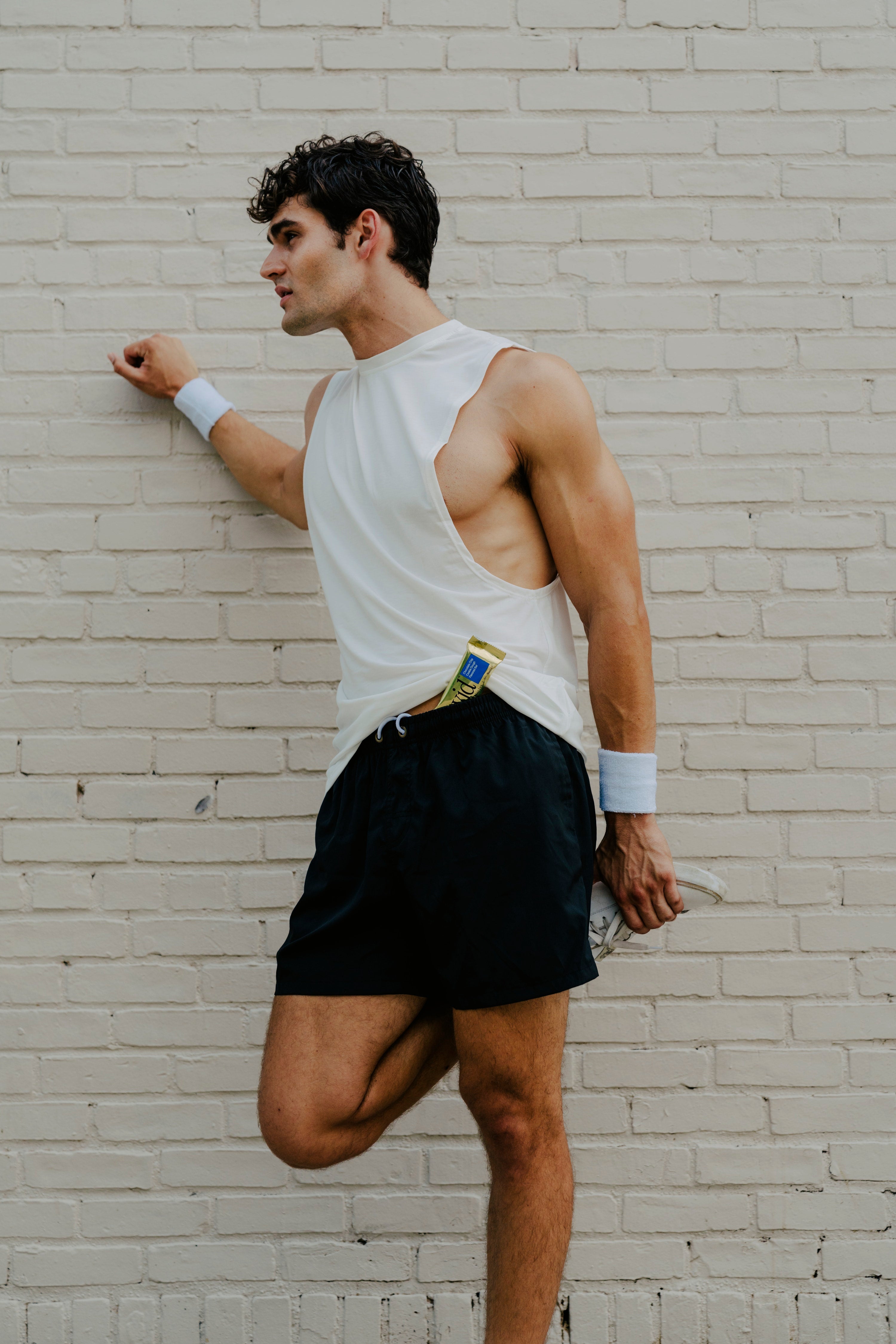 Man leaning against white wall with a David Protein Gold bar in his waist band